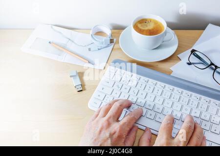 Hands using a computer keyboard on an office desk with coffee, usb stick and papers, business at home concept, copy space, selected focus, narrow dept Stock Photo