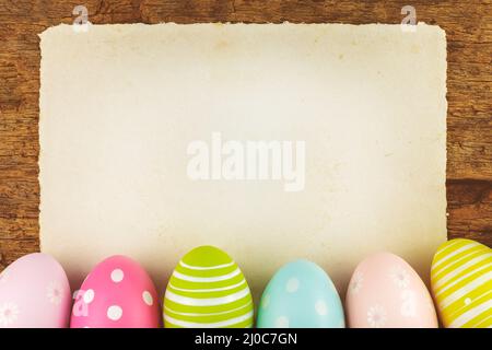 Colorful painted easter eggs in front of an old wooden background with blank paper sheet Stock Photo