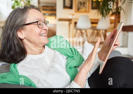 Happy senior woman video chatting with friends or family on tablet computer at home Stock Photo