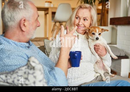 Happy senior couple with small dog having relaxed conversation on sofa at home, Stock Photo