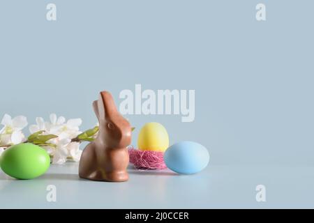 Easter chocolate rabbit in spring composition with colorful eggs on blue background. Happy Easter greeting card. Stock Photo