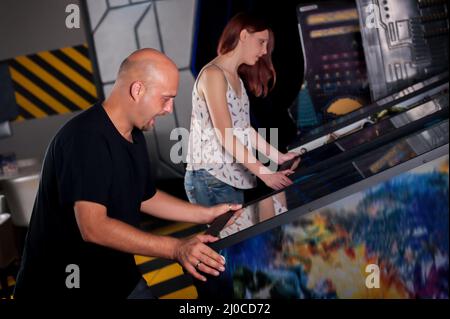 People playing pinball at arcade in game room Stock Photo