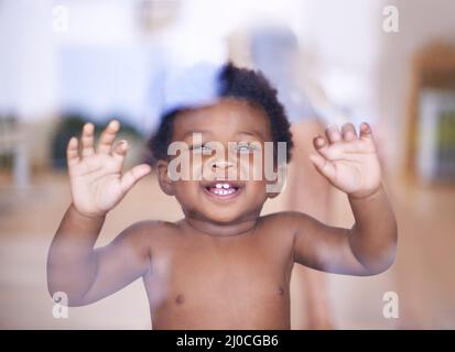 Im ready to go outside and play now. Shot of a cute baby boy looking through a window. Stock Photo