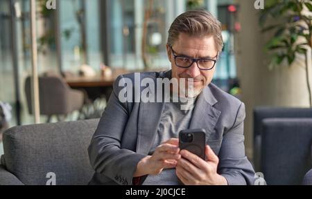 Businessman using phone in office lobby or on cafe terrace. Happy middle aged man, entrepreneur, small business owner working online. Stock Photo