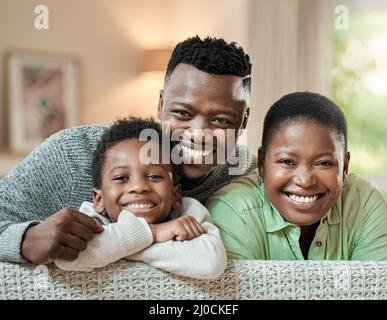 Hes got us smiling from ear to ear. Cropped portrait of an affectionate young family of three relaxing on the sofa in their living room at home. Stock Photo