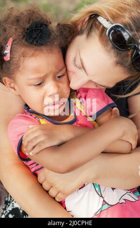 Sad little girl cries in park. Mother calms her kissing on cheek Stock Photo