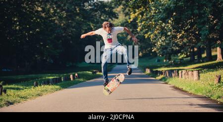 Action shot of a skateboarder skating, doing tricks and jumping on the road through the forest. Free riding skateboard Stock Photo