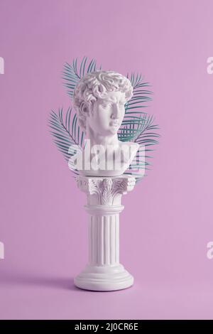 Pure white Grecian or Roman style bust backed by fronds or leaves on an ornate pedestal over a pink background in vertical format Stock Photo
