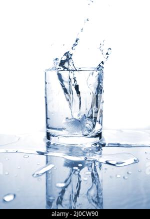 Drinking water splashed with ice in glass on white background with reflections. Stock Photo