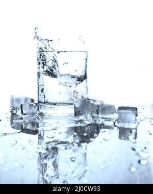Drinking water splashed with ice in glass on white background with reflections. Stock Photo