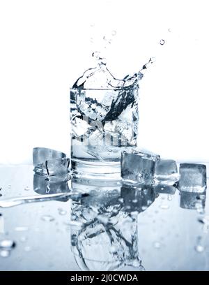 Drinking water splashed with ice in glass on white background with reflections. Stock Photo
