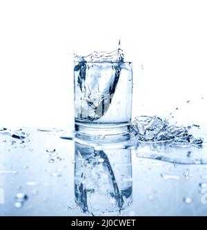 Drinking water splashed with ice in glass on white background with reflections. Stock Photo