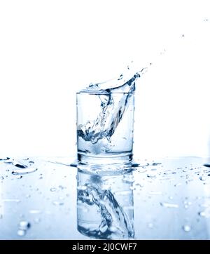 Drinking water splashed with ice in glass on white background with reflections. Stock Photo