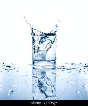 Drinking water splashed with ice in glass on white background with reflections. Stock Photo
