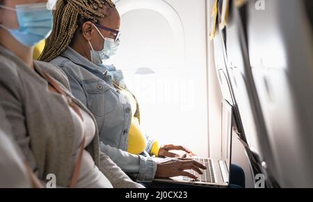 Senior woman using laptop during airplane trip while wearing face mask Stock Photo
