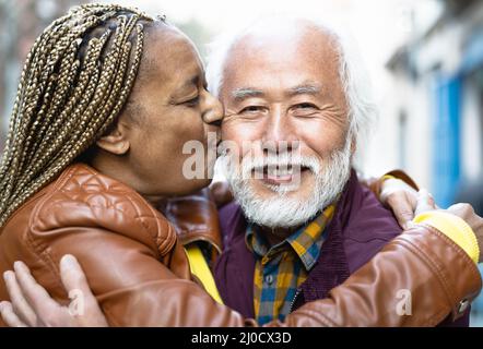 Happy multiracial senior couple having tender moments in city - Elderly people and love relationship concept