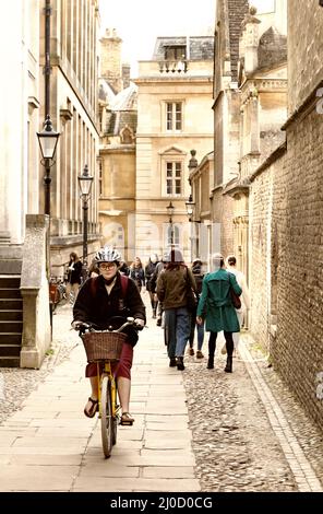 Cambridge street scene; Cambridge University student riding a bicycle, cycling in Senate House Passage, Cambridge city centre, Cambridge UK Stock Photo