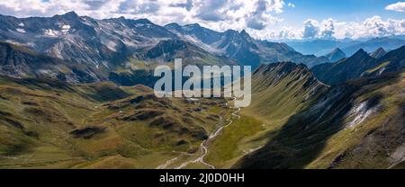 Aerial pano view towards Capanna Motterascio, an alpine hut on the Greina plateau in Blenio, Swiss Alps. A rocky ridge on the right leads the eye towards the river that flows sinuously in the valley. Stock Photo