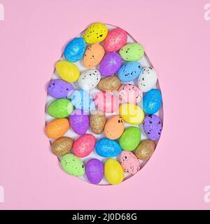 Easter egg shape frame filled with colorful eggs on pastel pink background. Flat lay Stock Photo