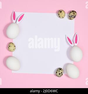 White paper card copy space with white and quail eggs on paper on pastel pink background. Flat lay Stock Photo