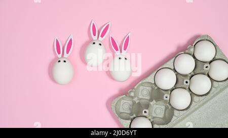 Card box with white natural eggs and eggs with rabbit ears on pastel pink background. Flat lay Stock Photo