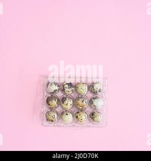 Plastic box and quail natural eggs in it on pastel pink background. Flat lay Easter concept Stock Photo