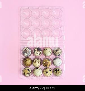 Plastic box and quail natural eggs in it on pastel pink background. Flat lay Easter concept Stock Photo