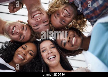 Enjoying campus life. Low angle shot of young university students standing arm in arm on the school campus. Stock Photo