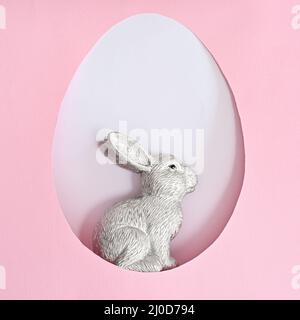 Easter ceramic bunny rabbit in egg shape frame on pastel pink and white background. Creative spring holidays concept Stock Photo