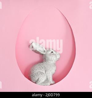 Easter ceramic bunny rabbit in egg shape frame on pastel pink background. Creative spring holidays concept Stock Photo