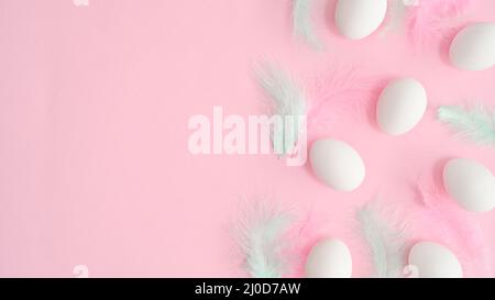 Romantic pastel pink background with white natural eggs and bright feathers. Creative copy space flat lay. Easter composition Stock Photo