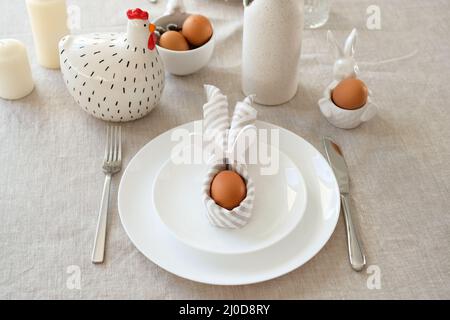 Cute Easter table setting. Easter egg in Easter bunny napkin on plate on linen tablecloth. Stock Photo