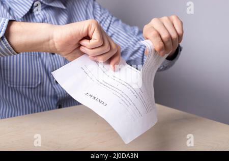 Man hands closeup tearing contract. Termination of partnership, deal concept. Man sitting at desk in office and tearing document. Worker firing. High quality photo Stock Photo