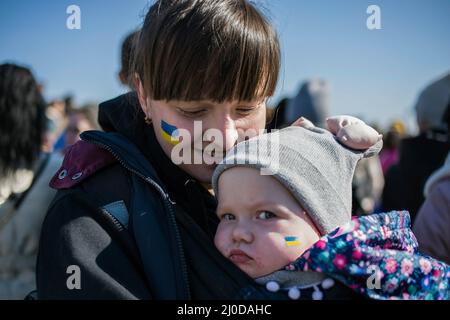 Warsaw, Poland. 18th Mar, 2022. A Ukrainian mother holds her baby with Ukrainian flag painted on her cheek during the protest. The 'March of Ukrainian Mothers' was held in Warsaw, which was also a protest against the war and killing of Ukrainian children. The slogans of the march were 'World, help our children', 'Stop the war', 'Save kids of Ukraine' and 'Close the sky'. Mainly Ukrainian mothers and their children, who found refuge in Poland from the war, took part in the protest. (Photo by Attila Husejnow/SOPA Images/Sipa USA) Credit: Sipa USA/Alamy Live News Stock Photo