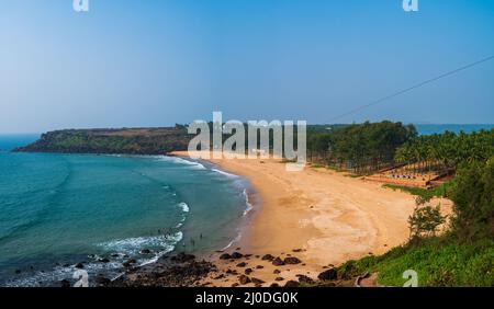 Sindhudurg, India - December  21, 2021 : Beautiful landscape of the Arabian sea with coconut trees, boys playing in sea and tents. Stock Photo