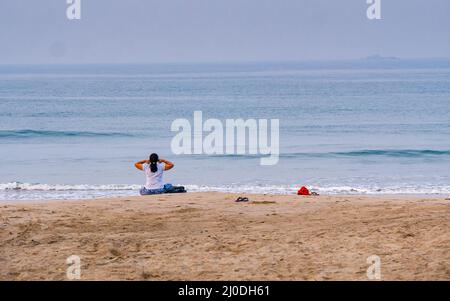 Sindhudurg, India - December  21, 2021 : Unidentified female performing yoga practices at seashore during morning time. Stock Photo