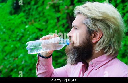 Bearded man drinking water from bottle outdoors. Hydration concept. Healthy lifestyle. Stock Photo