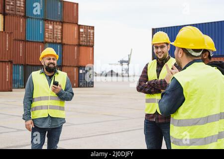 Multiracial industrial workers working inside international port terminal with shipping containers outdoor - Focus on latin man hand holding walkie ta Stock Photo
