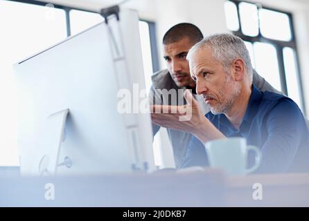 Giving some experienced advice. Shot of two colleagues having a discussion at a computer in the office. Stock Photo