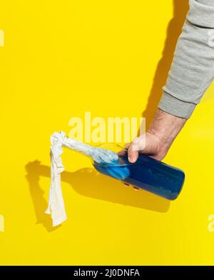Mans hand holding Molotov cocktail bottle full with blue liquid on yellow background. Minimal Ukraine concept. Stock Photo