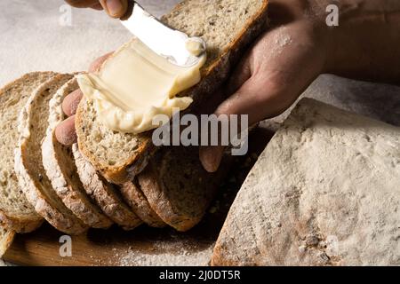 Man spreading cream cheese butter or a slice of bread slice on wood board. Dieting bread. Close-up. Healthy nutrition concept.  Stock Photo