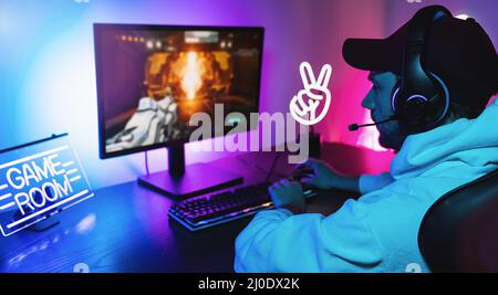Gamer Playing First-Person Shooter Online Video Game on His Powerful Personal Computer. Room and PC have Colorful Neon Led Lights. Young Man is gaming Stock Photo