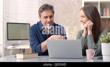 Business people working in office with laptop computer. Happy couple working from home at desk. Talking, meeting, cooperation, entrepreneurs, advisor. Stock Photo
