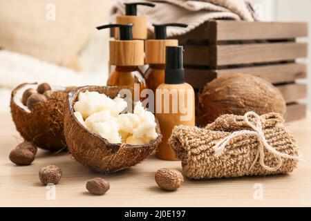 Coconut shells with shea butter, nuts and bath supplies on table in room, closeup Stock Photo