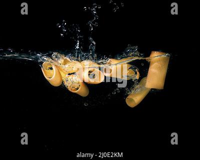 pasta rings falling in the boiling water on dark background. Underwater view. Cooking, cooking at home Stock Photo
