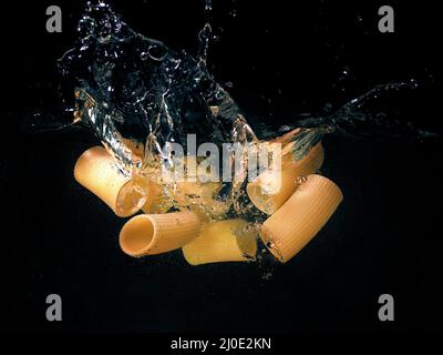 pasta rings falling in the boiling water on dark background. Underwater view. Cooking, cooking at home Stock Photo