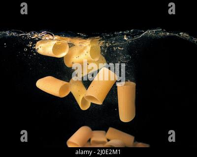 pasta rings falling in the boiling water on dark background. Underwater view. Cooking, cooking at home Stock Photo