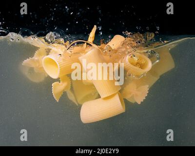 pasta rings falling in the boiling water on dark background. Underwater view. Cooking, cooking at home Stock Photo