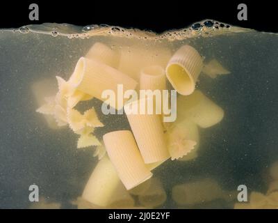 pasta rings falling in the boiling water on dark background. Underwater view. Cooking, cooking at home Stock Photo