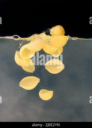 butterflies pasta falling in the boiling water on dark background. Underwater view. Cooking, cooking at home, italian cuisine concept Stock Photo